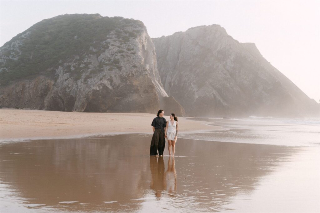 a lesbian couple standing side by side in scenic praia da adraga late afternoon