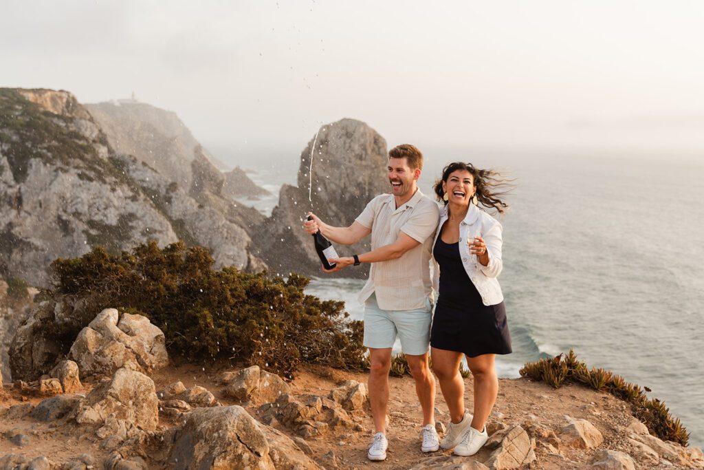 photo of a couple in scenic view above praia da adraga, Lisbon popping champagne