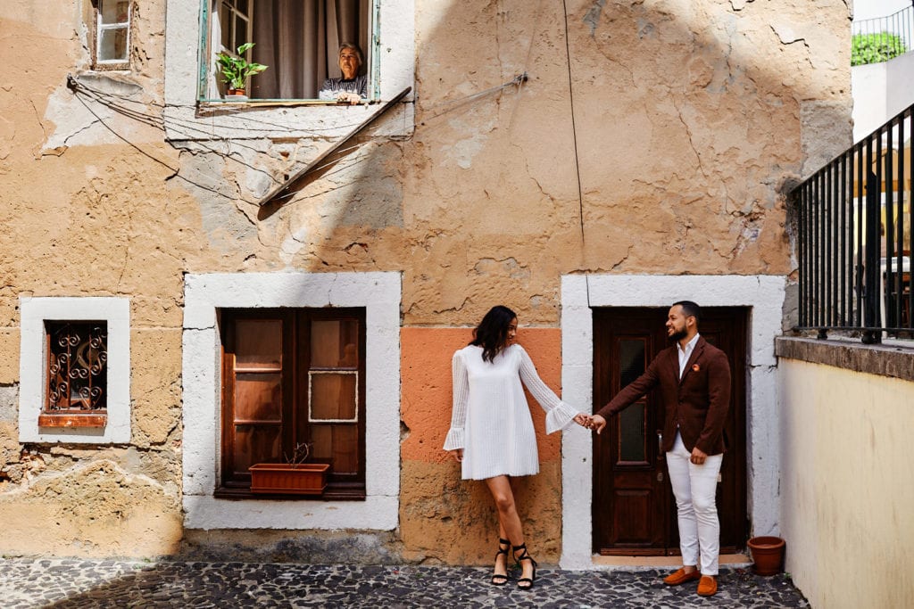 a couple holds hands under a window during their engagement shoot in Lisbon