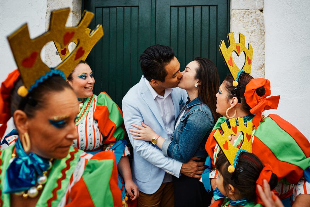 A couple kiss in front of a door in the middle of a number of women in costumes, in Alfama, in Lisbon, Portugal