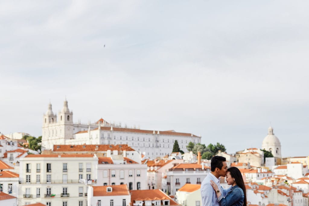 A couple hugs with Alfama's roofs as a backdrop during a romantic photo shoot in Lisbon