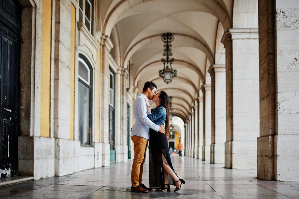 a couple kisses in Praça do Comercio as part of a romantic photoshoot after a marriage proposal in Lisbon, Portugal