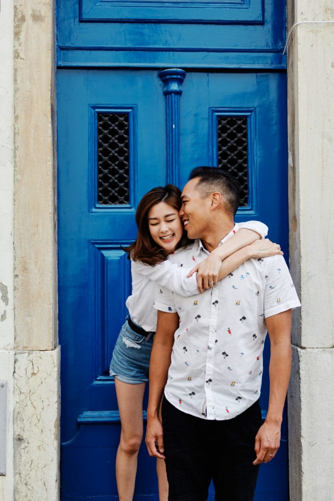 Eliza Sam and Joshua Ngo hug in front of a blue door in the mouraria neighbourhood in Lisbon, Portugal