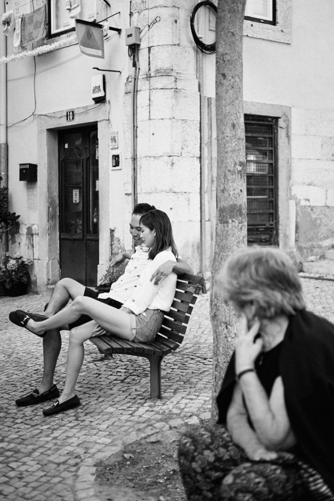 Eliza Sam and Joshua Ngo sit on a bench on the street in Lisbon