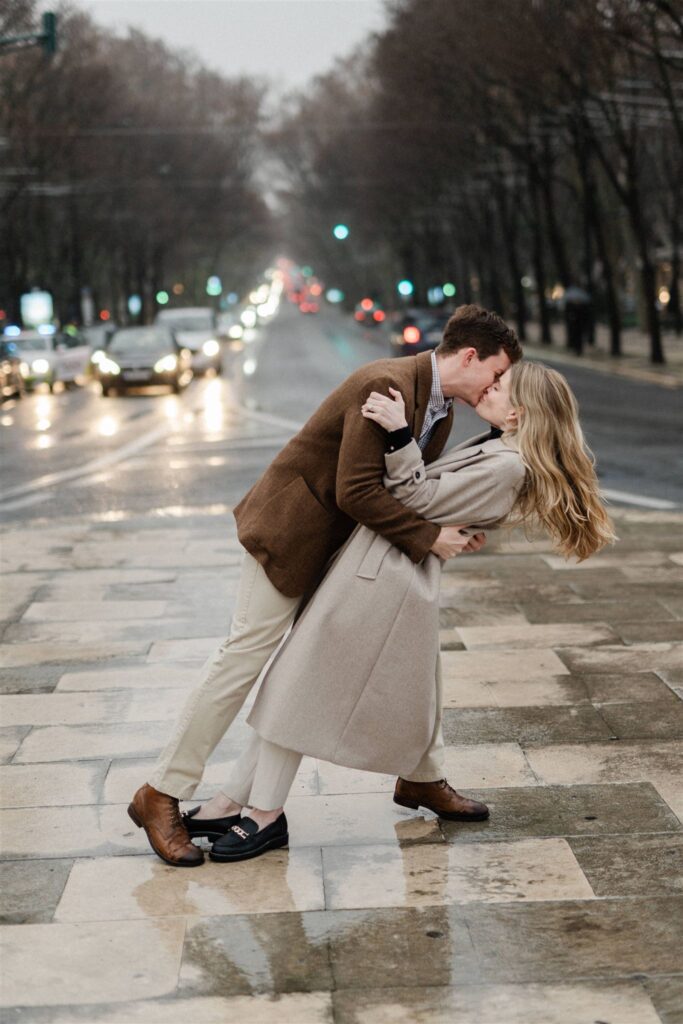 a couple kisses in the rain with the city lights behind as part of an engagement shoot in Lisbon, Portugal