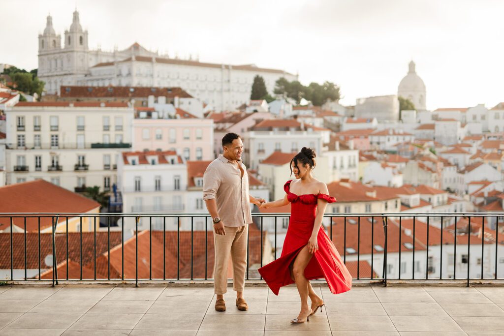A woman in a red dress dances with her fiancee early in the morning in Alfama during their Lisbon photoshoot