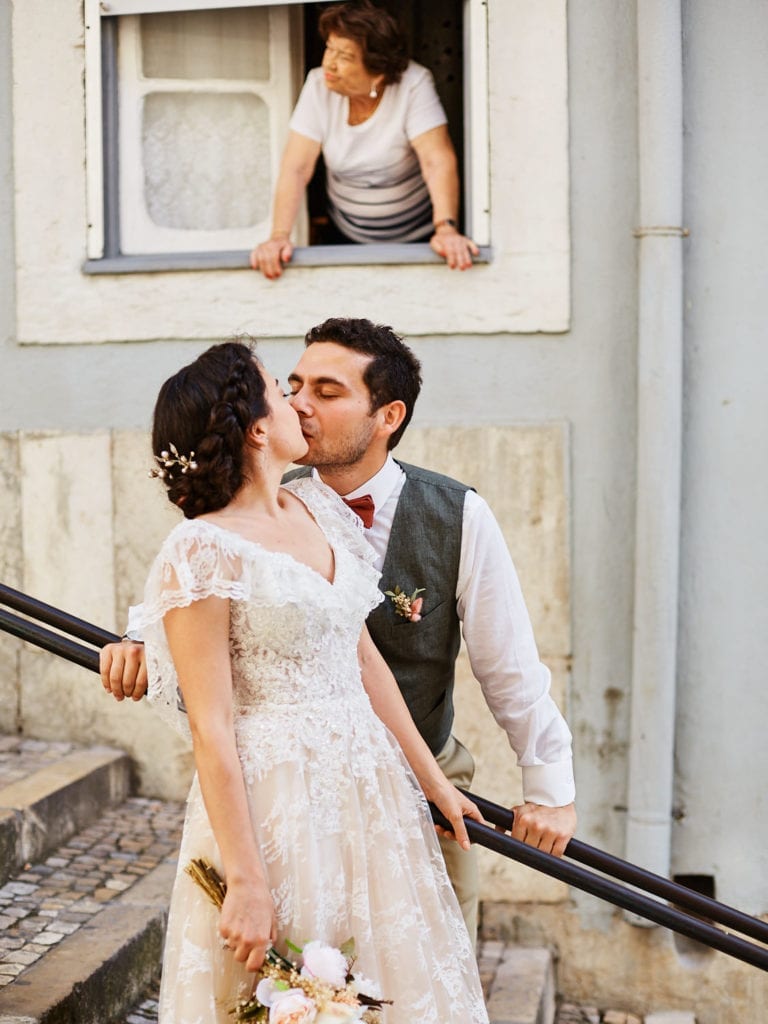 A newlywed couple in their wedding attire kisses in the street in Lisbon's Mouraria Neighbourhood