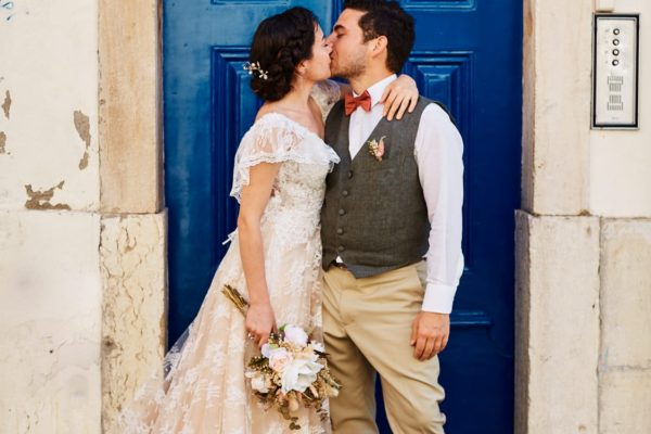 a newlywed couple kisses in Lisbon, Portugal, with a blue door as a backdrop, on their elopement in Lisbon