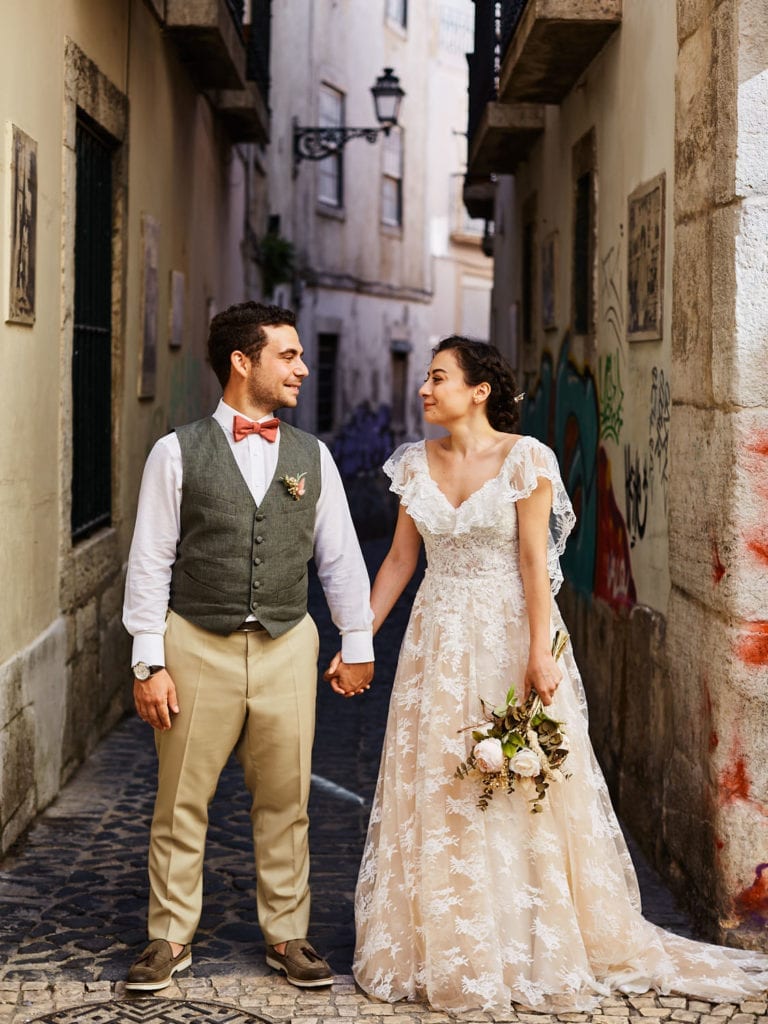 a newlywed couple look at each other hand in hand in the streets of Mouraria, Lisbon, Portugal