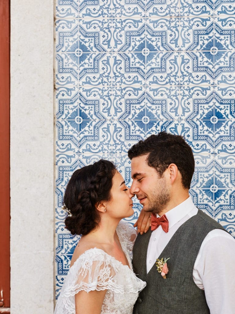 a bride and a groom pose nose to nose with their eyes closed on a backdrop of azulejos or painted Portuguese tiles, on their elopement in Lisbon