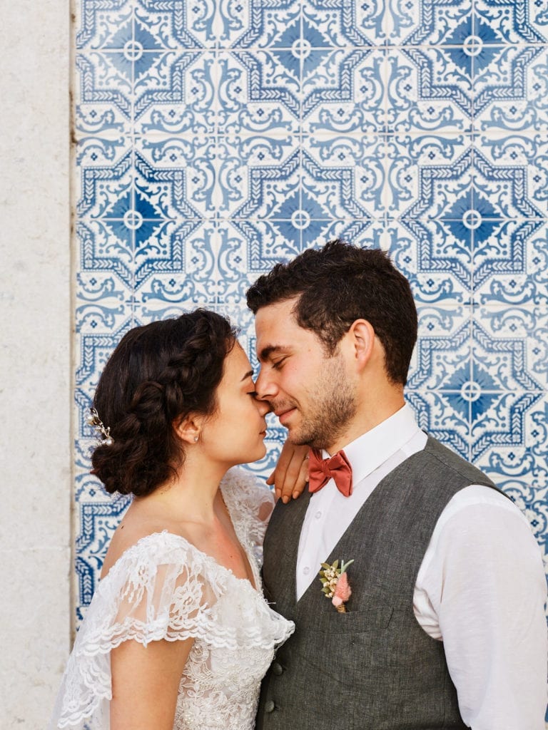 a bride and a groom pose romantically against a wall of painted tiles on their elopement in Lisbon, Portugal