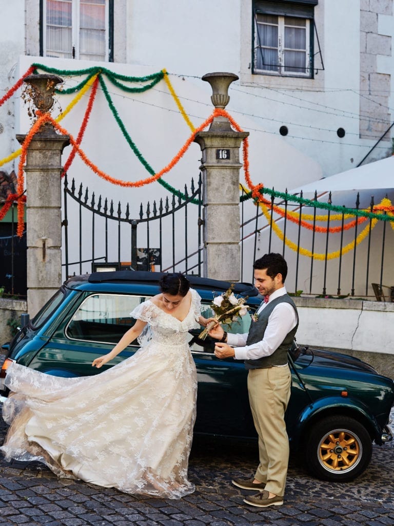 a newlywed couple in their wedding attire in a candid moment, near a Mini Cooper in Alfama, Lisbon, Portugal, on their elopement