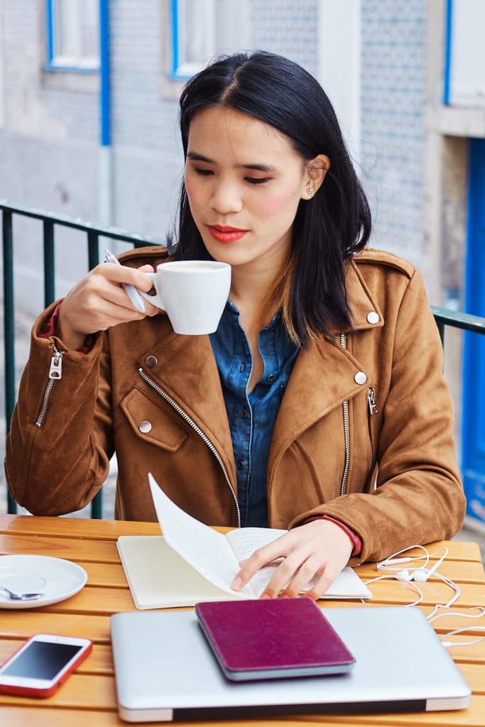 a girl drinks cappuccino at a café in Lisbon while looking at her notes