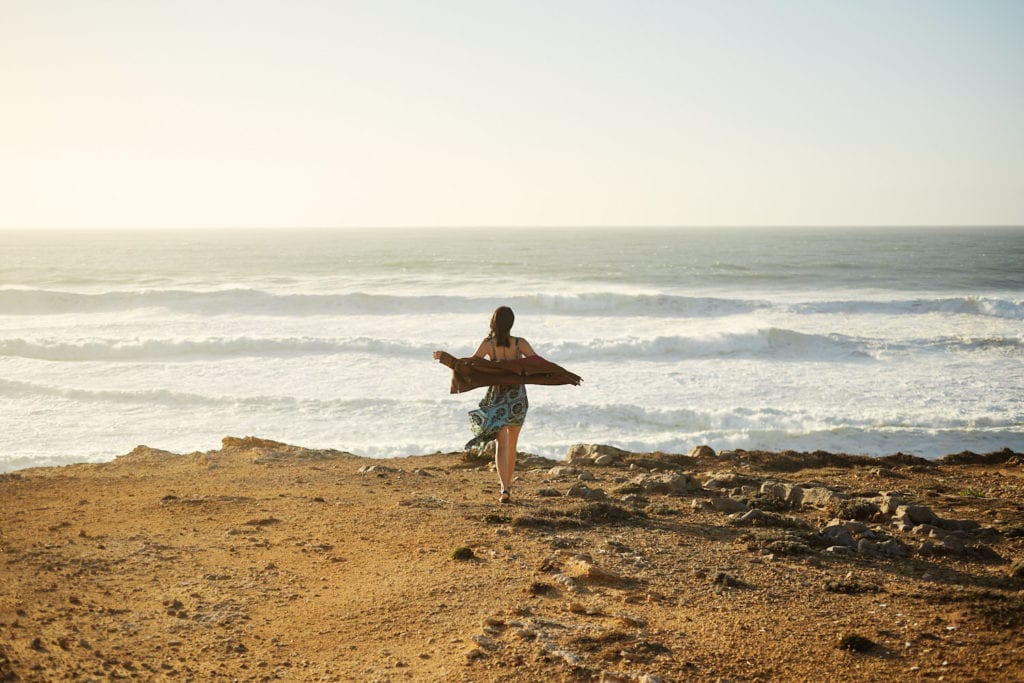 a girl walks toward the edge of a cliff in Guincho beach, near Cascais, Lisbon, Portugal as part of a professional photo session with Lisbon Photographer Your Story in Photos